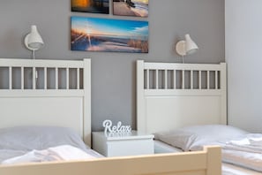 A bedroom with two beds, a nightstand, and wall-mounted lamps.