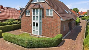 A red brick house with a gabled roof, large windows, and a well-maintained hedge. - Gode Stuuv - Our "good room" (75sqm) for 4 persons centrally located in Greetsiel (Krummhörn)