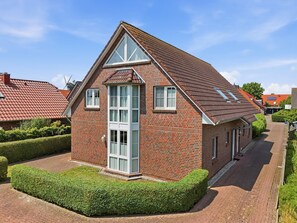 A red brick house with a gabled roof, large windows, and a well-maintained hedge.