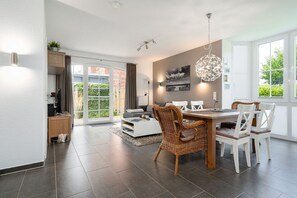 A modern living room with a dining area, a fireplace, and a large window. - Gode Stuuv - Our "good room" (75sqm) for 4 persons centrally located in Greetsiel (Krummhörn)