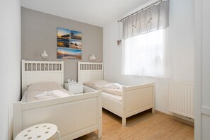 A child's bedroom with two beds, a small table, and a window with curtains. - Gode Stuuv - Our "good room" (75sqm) for 4 persons centrally located in Greetsiel (Krummhörn)