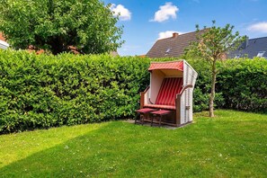 A garden with a wicker chair and table, surrounded by well-maintained hedges and a house in the background. - Gode Stuuv - Our "good room" (75sqm) for 4 persons centrally located in Greetsiel (Krummhörn)