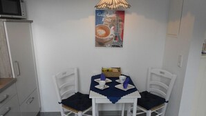 Un pequeño comedor con una mesa dispuesta para dos comensales, sillas blancas, mantel azul y una lámpara fijada a la pared.
