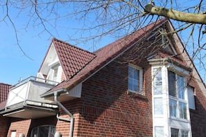 Ein zweistöckiges Backsteinhäuschen mit rotem Ziegeldach, einem sichtbaren Schornstein und einem Fenster mit Fensterläden.