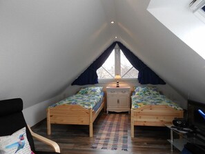 Ein kleines Schlafzimmer im Dachgeschoss mit zwei Holzbetten, einem Nachttisch, einer Lampe und einem Fenster mit Vorhängen.