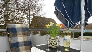 Un balcón con una silla de cuadros, una mesita pequeña, dos copas de vino y una botella.