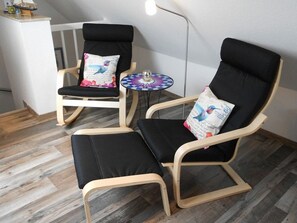 Ein Zimmer mit zwei schwarzen Sitzgelegenheiten mit Holzrahmen, einem kleinen runden Tisch mit farbigem Muster und einer Stehlampe.