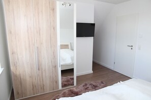 Ein Schlafzimmer mit Holzschrank, einem Bett mit weißer Bettwäsche, einem flauschigen Teppich und einem Wand-Fernseher.