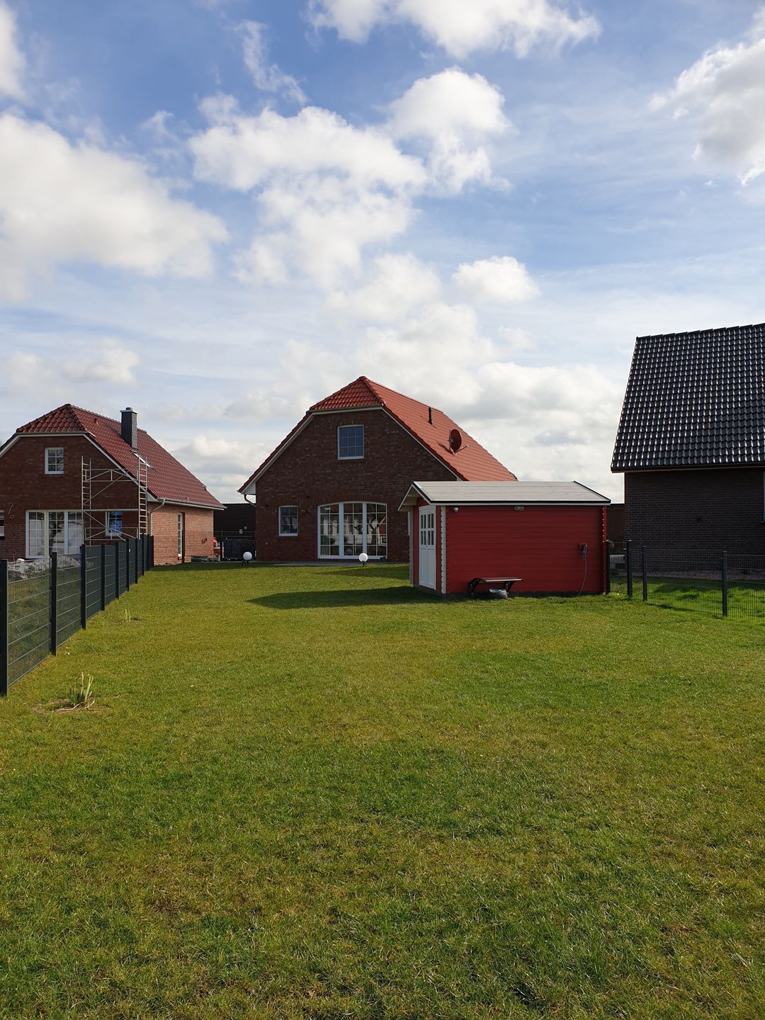 A residential area with brick houses, a red garage, and a fenced yard.