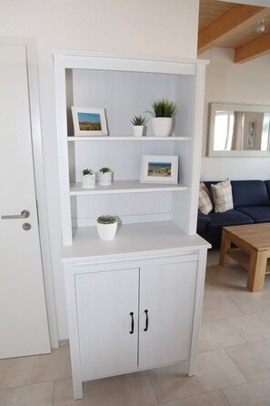 A white cabinet with two doors and three shelves, each holding framed pictures and small potted plants.