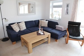 Ein Wohnzimmer mit einem dunkelblauen Sofa, einem Holztisch, einem schwarzen Ledersessel und einer Stehlampe.