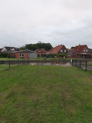 A residential area with houses, a small pond, and a fenced grassy area. - Bei Ruhe - Beautiful vacation home in a fantastic waterfront location (Hinte)