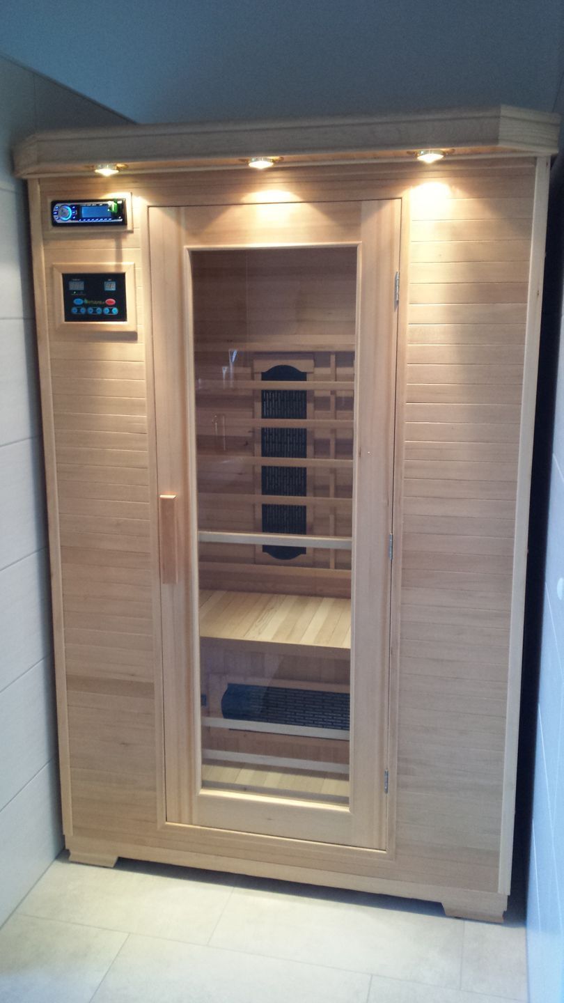 Una sauna de madera con un panel de control a la izquierda, un banco en el interior y suelo de baldosas.