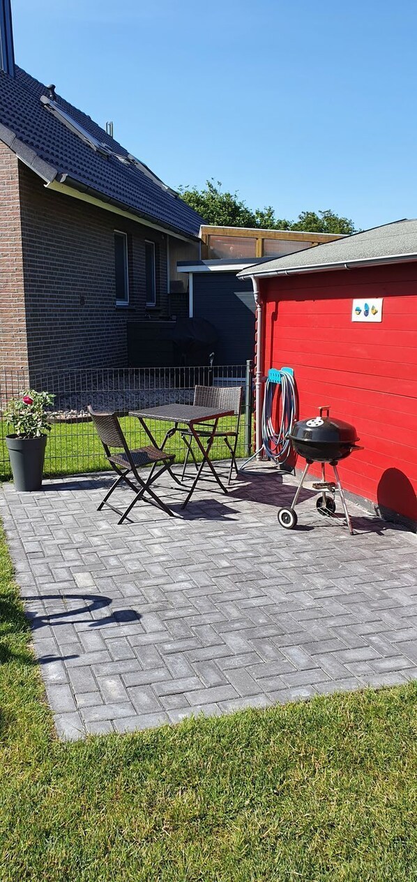 Une terrasse avec un barbecue, des chaises pliantes et un abri de jardin rouge.