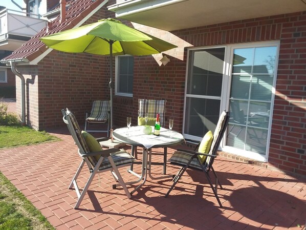 A patio with a table and chairs, a green umbrella, and a brick wall.