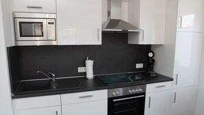 Moderni keittiö, jossa on mikroaaltouuni, liesi, uuni ja kahvinkeitin.