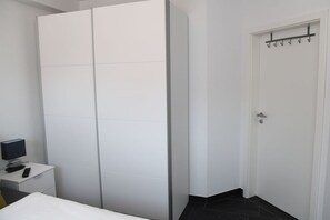 Un dormitorio con un armario blanco, una mesita de noche con una lámpara y una puerta con perchero.