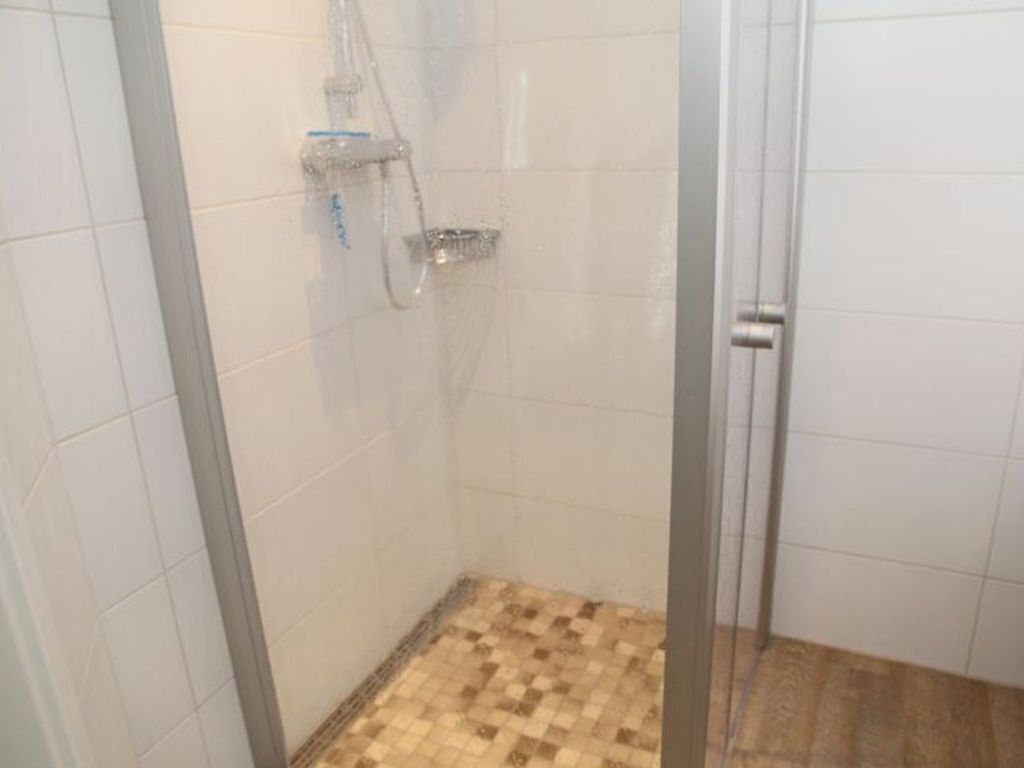 A glass-enclosed shower with a tiled floor, a showerhead, and a control panel.