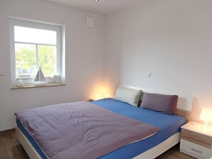 Une chambre à coucher avec un lit, des tables de chevet, une fenêtre et une vue sur la verdure.