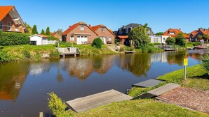 A canal with houses on one side and a wooden dock on the other. - Leo - Schöne Erdgeschosswohnung mit Hund in Wassernähe (Krummhörn)