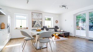 A modern living room with a dining area, large windows, and a view of the outdoors. - Leo - Schöne Erdgeschosswohnung mit Hund in Wassernähe (Krummhörn)
