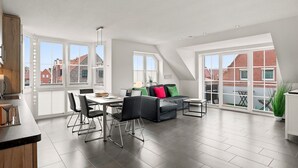 Un vaste appartement de style « loft » comprenant un coin repas, un ensemble de canapés et de grandes fenêtres offrant une vue sur la ville.