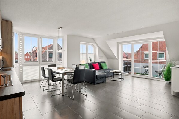 A spacious loft apartment with a dining area, a sofa set, and large windows offering views of the city. - Meerzeit - Schöne Obergeschosswohnung mit Wasserzugang (Krummhörn)