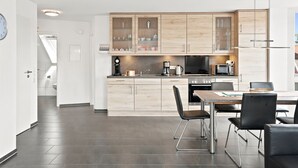 Une cuisine moderne avec des meubles en bois, un coin repas comprenant une table et des chaises, et une horloge visible au mur.