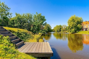A wooden deck by a calm river with a bridge in the background and a building with a red roof. - Frieso am Siel - Frieso am Siel - Holiday apartment with a view of the Siel in Greetsiel (Krummhörn)