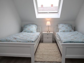 Une chambre avec deux lits, une petite table de chevet avec une lampe, un sol recouvert d’une moquette et une lucarne.