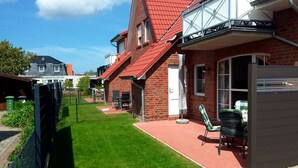 A residential building with a red roof, brick exterior, and a small patio with outdoor furniture.