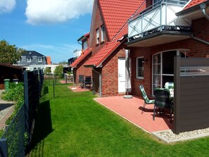 Un immeuble résidentiel avec un toit rouge, une façade en briques et un petit patio aménagé avec du mobilier d’extérieur.