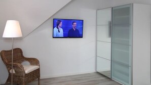 A modern room with a flat-screen TV mounted on the wall, a wicker chair with a cushion, and a glass cabinet.