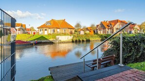A canal with houses on the opposite bank, a wooden dock, and a metal staircase leading down to the water.
