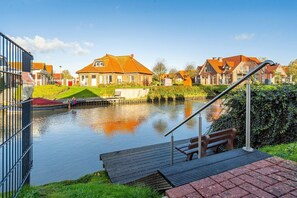 Un canal con casas en la orilla opuesta, un muelle de madera y una escalera metálica que baja al agua.