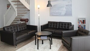 A modern living room with a staircase, leather sofas, a round coffee table, and a large abstract painting on the wall.