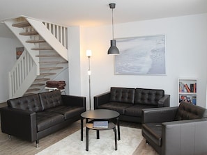 Un salon moderne avec un escalier, des canapés en cuir, une table basse ronde et un grand tableau abstrait accroché au mur.
