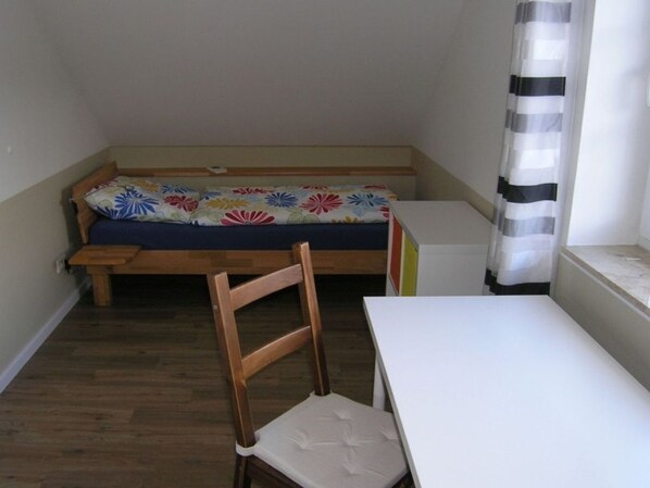 A small room with a wooden bench, a white table, and a colorful floral bedspread.