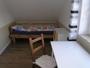 Una habitación pequeña con un banco de madera, una mesa blanca y una colcha de flores coloridas.