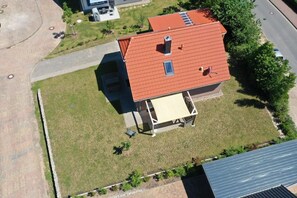 Vista aérea de una casa con techo rojo, un porche cubierto y un pequeño jardín.