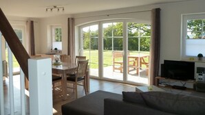 A spacious living area with a sofa, a dining table with chairs, a TV, and a large sliding glass door leading to an outdoor patio. - MaiStern - High-quality vacation home (100sqm) for 6 people with fireplace, sauna & (Sternberg)