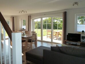 A spacious living area with a sofa, a dining table with chairs, a TV, and a large sliding glass door leading to an outdoor patio.