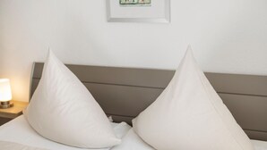 Ein Bett mit zwei weißen Kissen, einer Nachttischlampe und einem gerahmten Bild an der Wand.