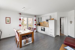 Una cucina moderna con mobili bianchi, un tavolo da pranzo con sedie e un divano rosso in una stanza luminosa con vista.