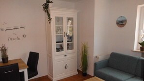 Un salon avec un canapé bleu, une table basse en bois, un meuble avec des portes en verre et un mur orné d’une boussole et du mot « Inseln ».