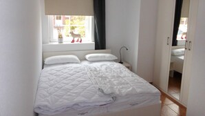 Une chambre à coucher avec un lit, une fenêtre avec des rideaux, une table de chevet avec une lampe et une armoire.