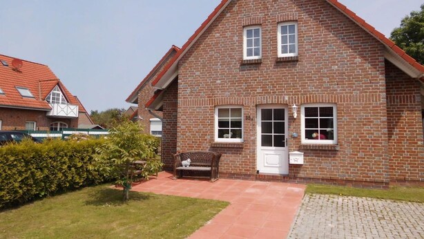 Une maison à deux étages, construite en briques et coiffée d’un toit rouge, avec un porche à l’avant doté d’un banc et un petit jardin.