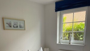 Una cama doble con ropa blanca, una lámpara de noche, un cuadro en la pared y una ventana con vistas a la vegetación.