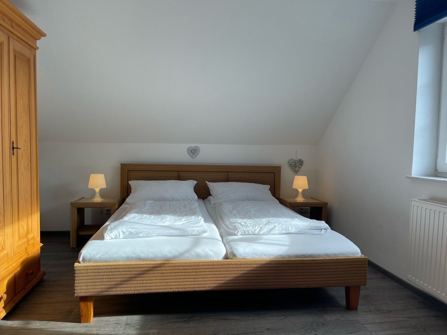 A bedroom with a wooden bed, two bedside tables with lamps, a wardrobe, and a window.