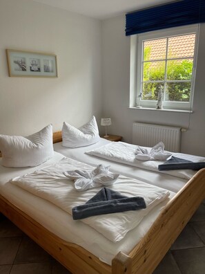 A double bed with white linens, a bedside lamp, a framed picture on the wall, and a window with a view of greenery. - Deichbrise - Deichbrise Vacation Home: A Relaxing Family Vacation in Greetsiel with (Krummhörn)